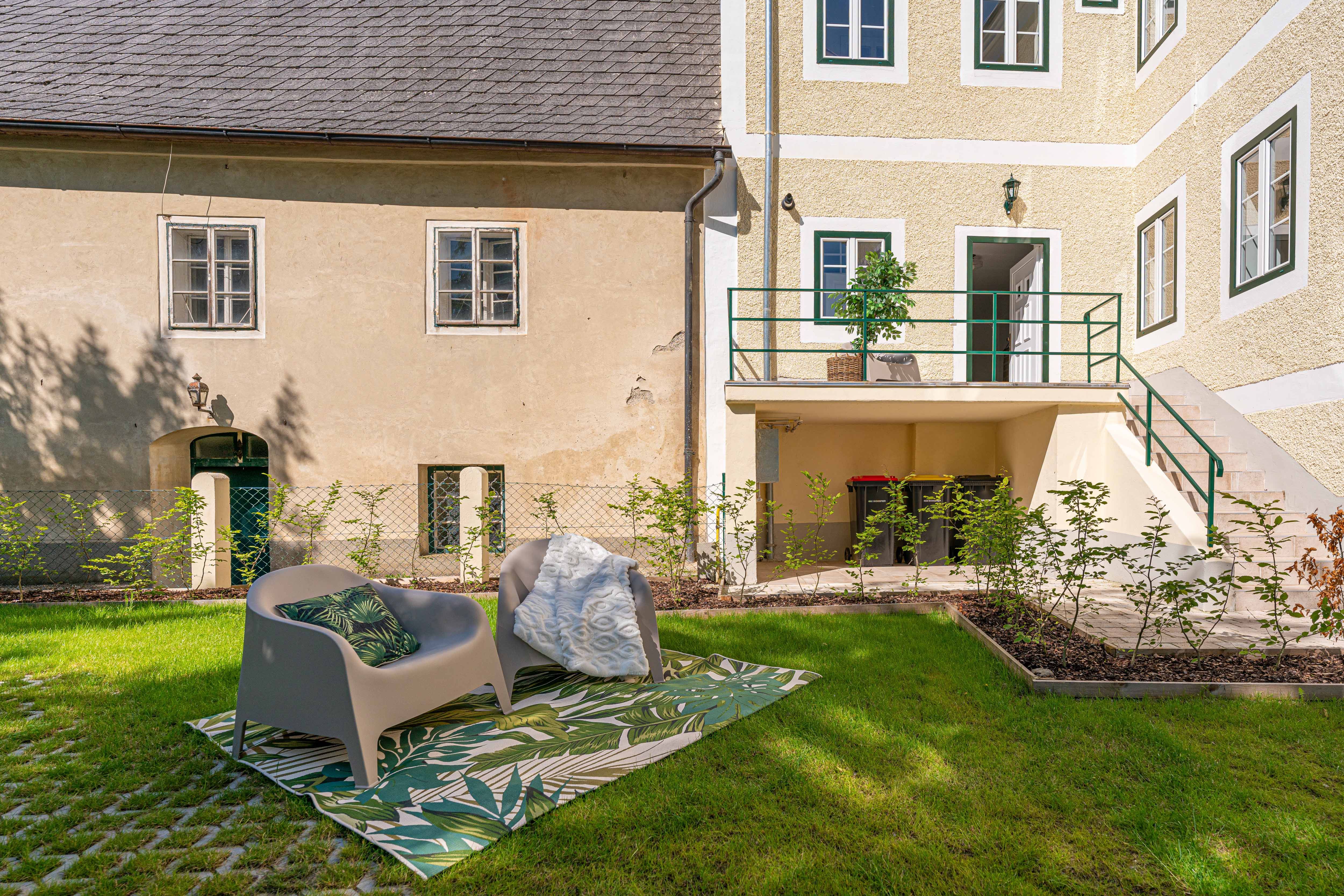 Garden with seating in front of an old building with a yellow façade and green window frames.