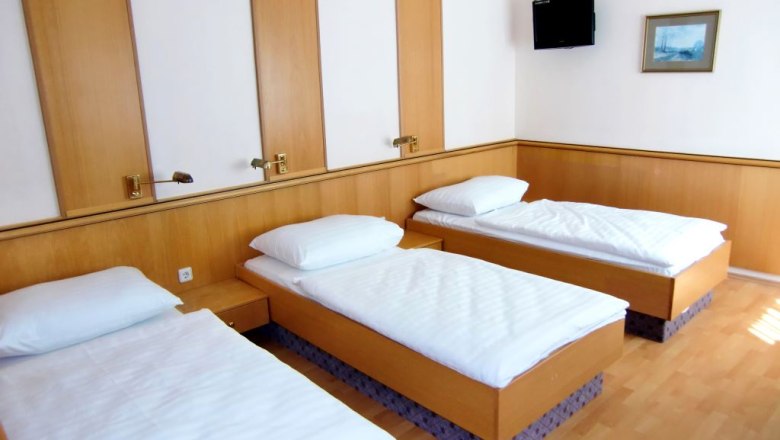 Triple room with three single beds, wooden walls, TV and picture on the wall.