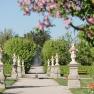 A well-kept garden path with statues and blossoming trees in spring.