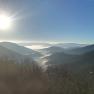 View from a mountain of mist-covered valleys and hills under a bright blue sky with sunshine.