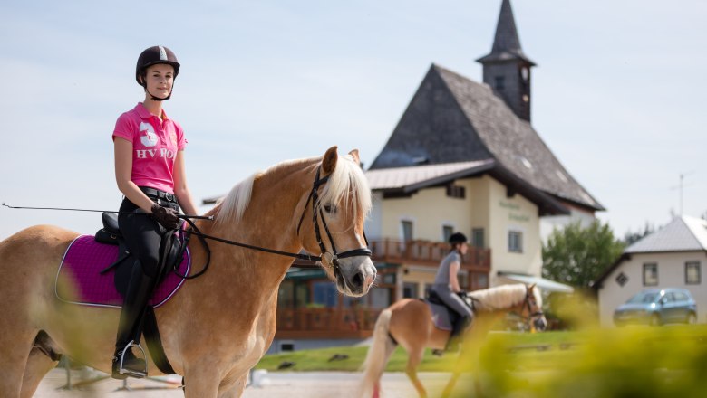 Two female riders on horses in front of a building with a tower.