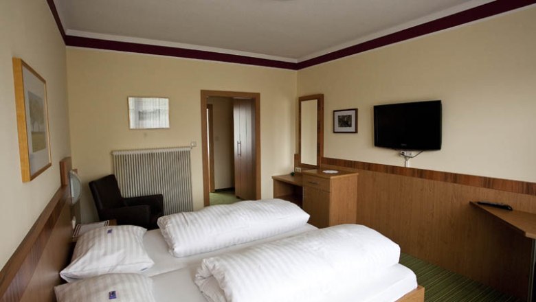 Hotel room with double bed, TV, desk and mirror.