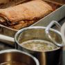Crispy roast pork in a metal pan, pots of gravy next to it.