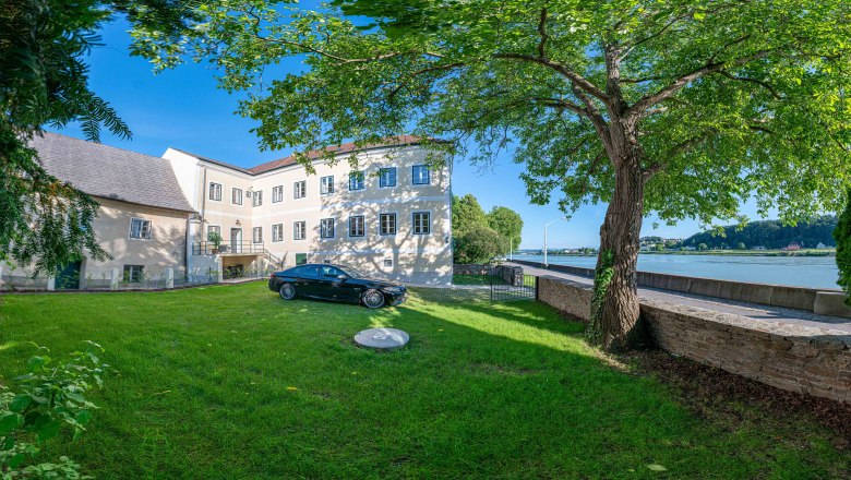 Exterior view of an old post office with tree and car in the foreground, Danube in the background.