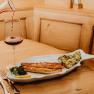 A plate with pike-perch fillet and potatoes in garlic butter, next to it a glass of red wine on a wooden table.