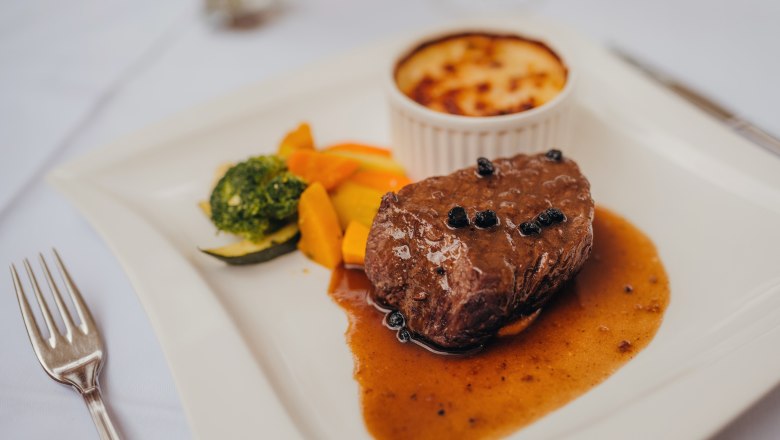A pepper steak with sauce, vegetables and potato gratin on a white plate.