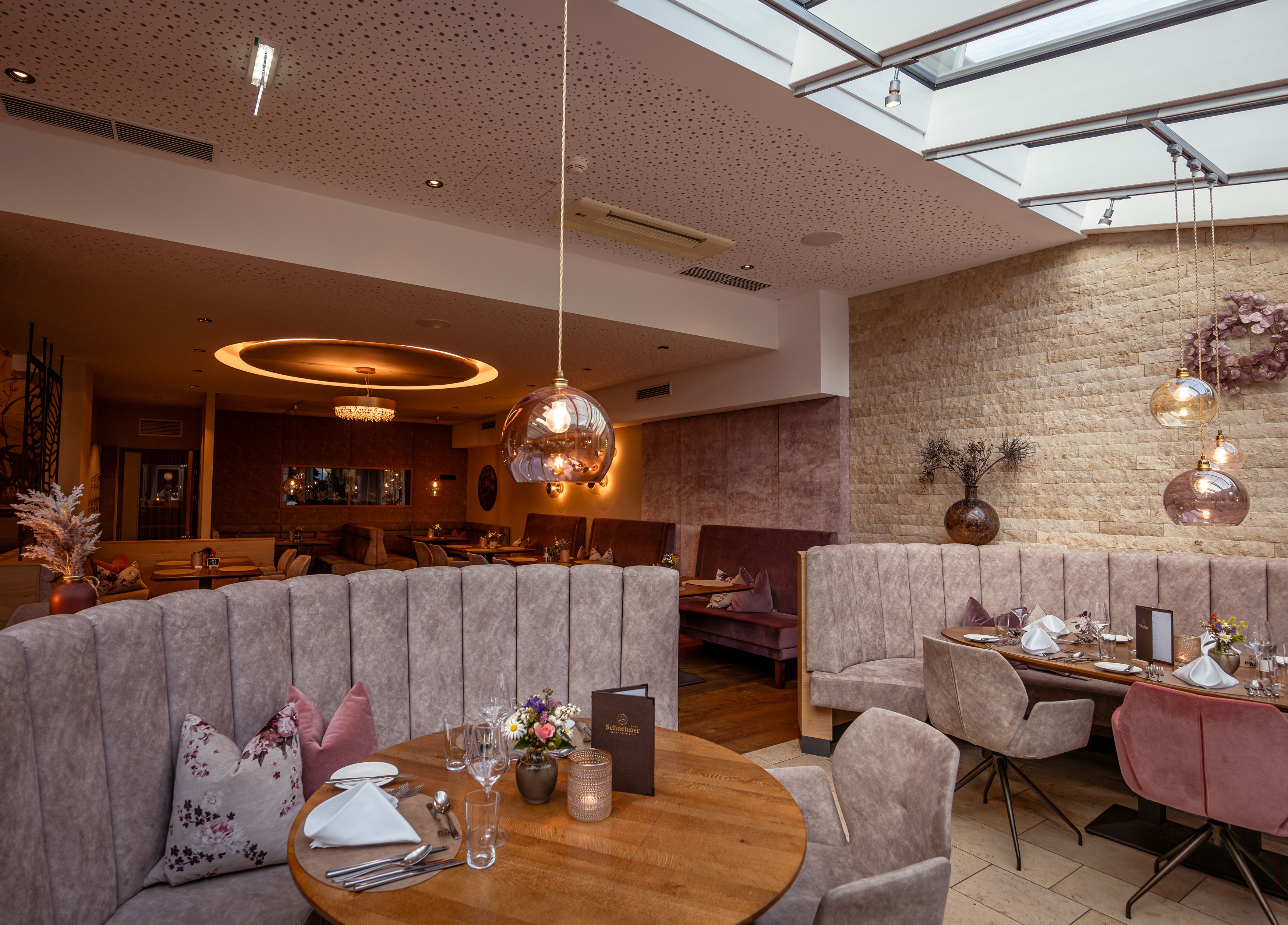 Elegant restaurant with modern furnishings, round tables and upholstered benches under a glass roof.
