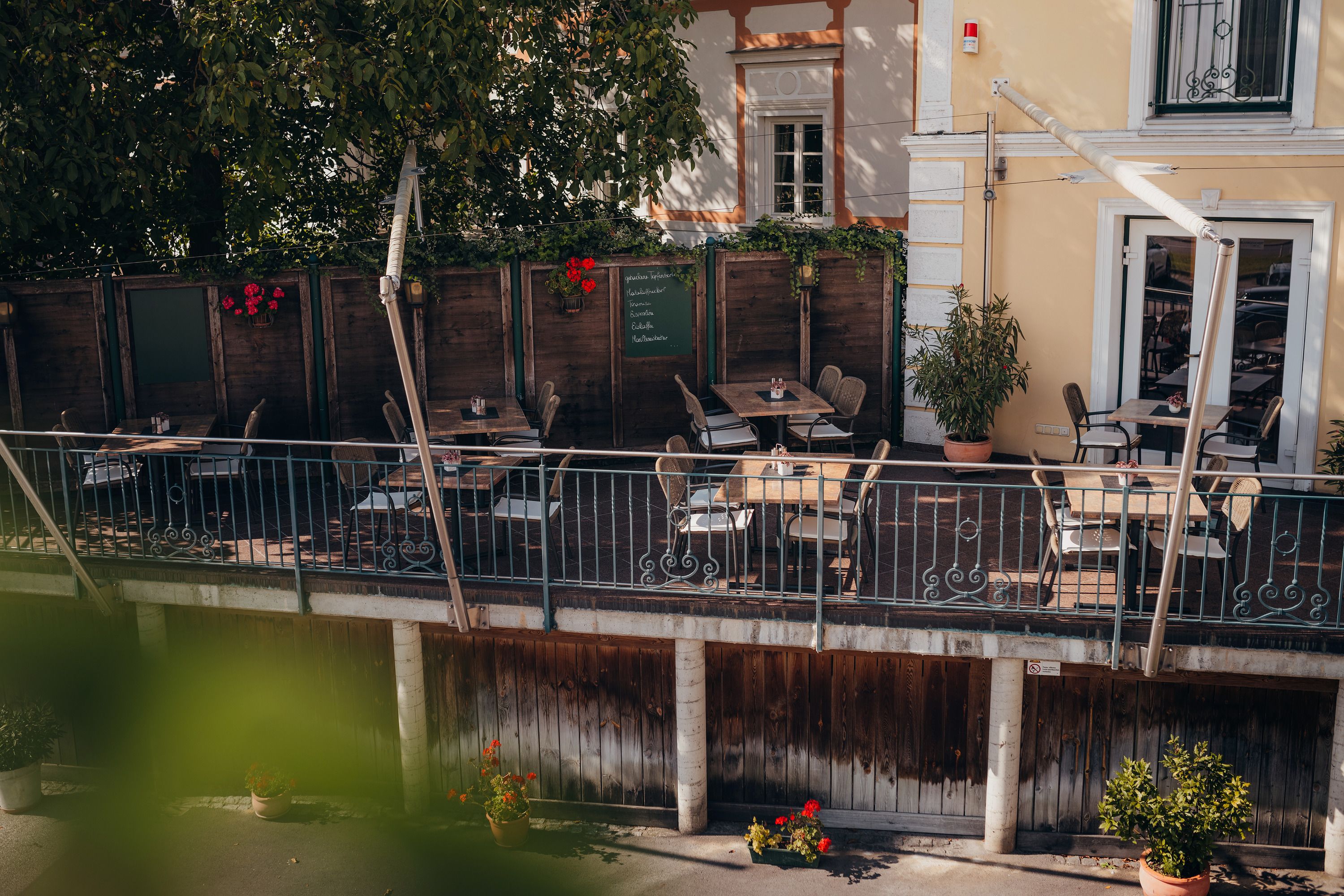 Cozy terrace of a café with wooden tables and chairs, surrounded by plants.