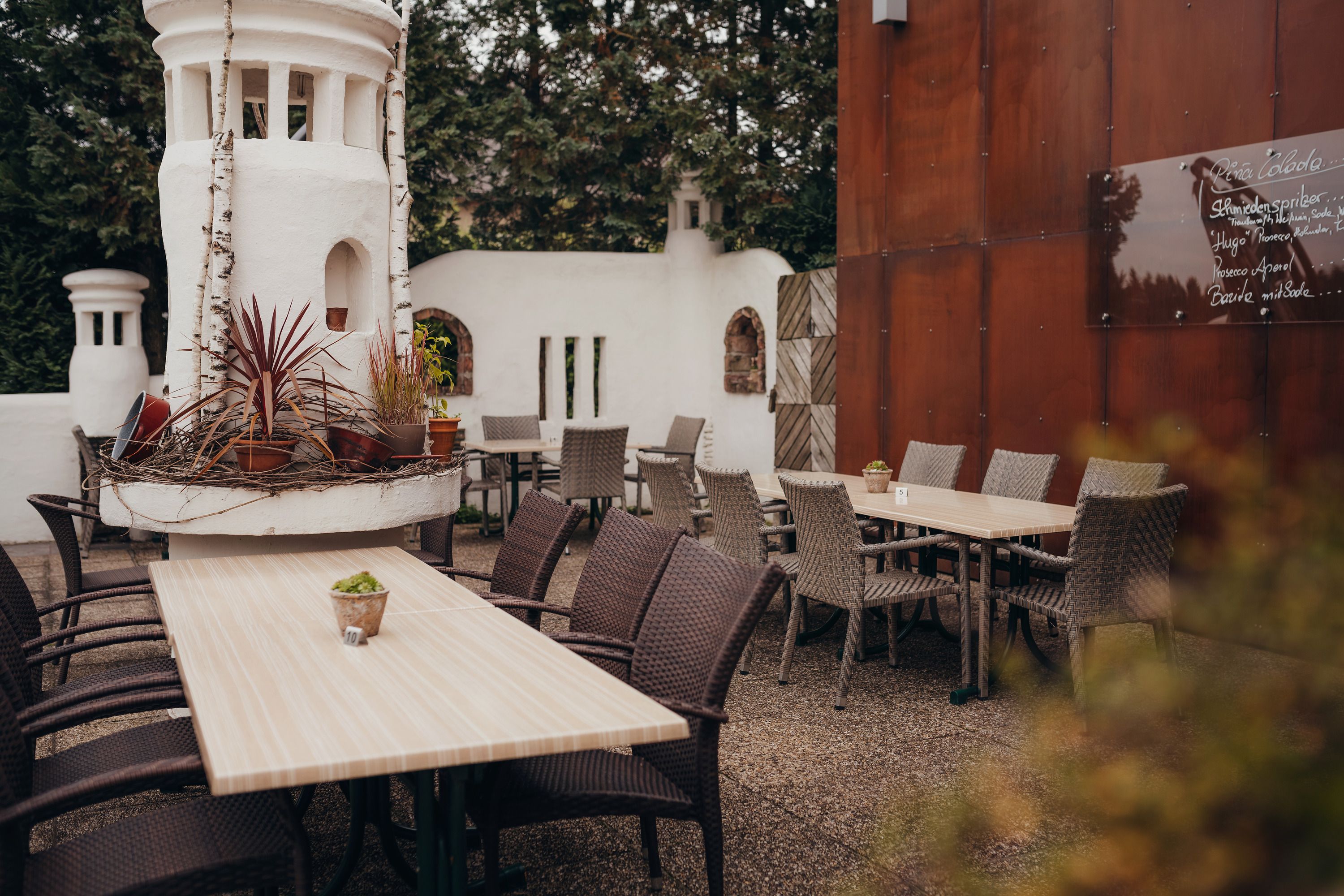 A cozy guest garden with wooden tables, woven chairs and decorative plants in a white tower.