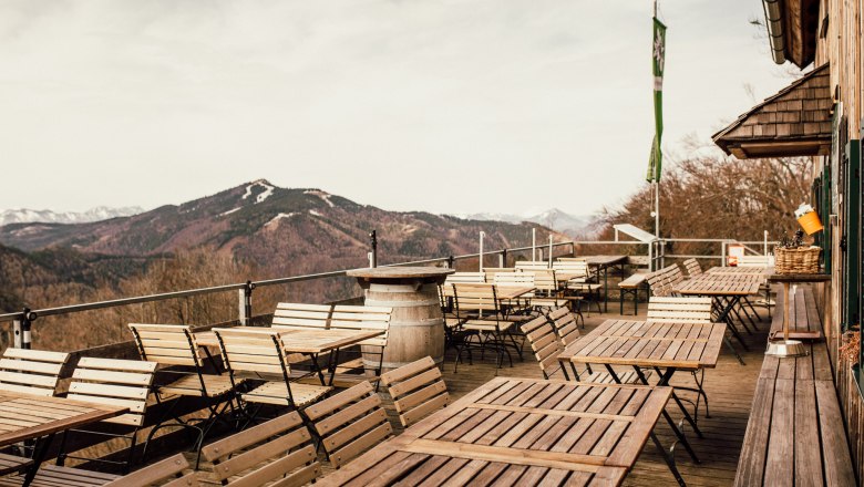 Empty terrace with wooden tables and chairs, mountain landscape in the background.