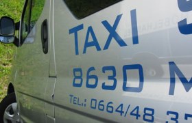 Close-up of a silver cab with blue lettering and telephone number.