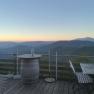 Terrace with wooden furniture and mountain views at sunrise.