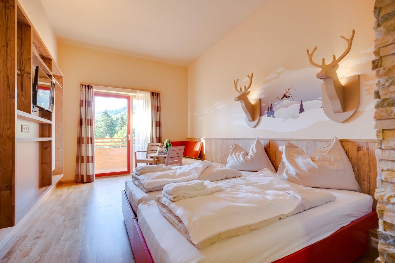 Hotel room with double bed, wooden furniture and balcony with mountain view.