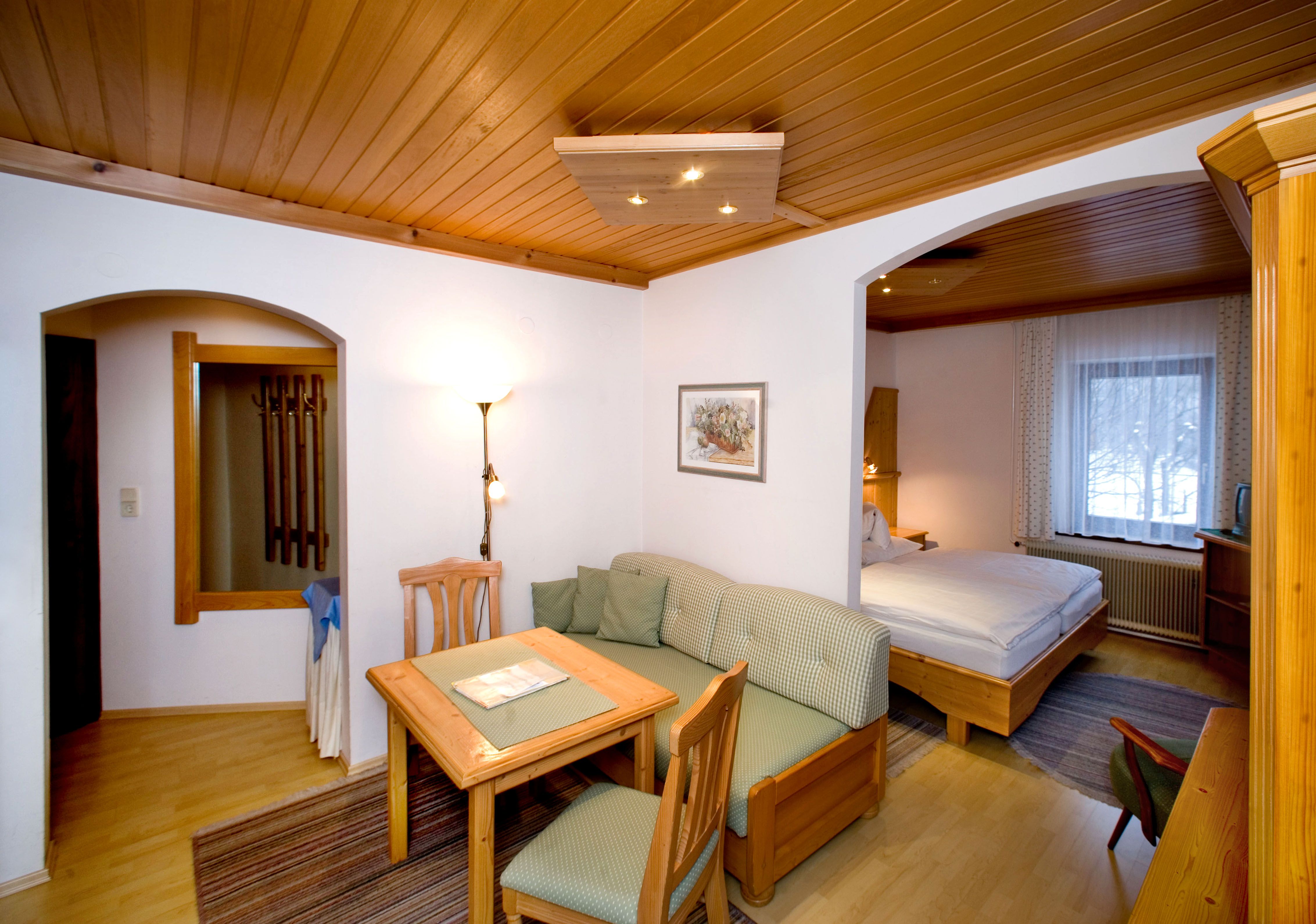 Comfortable hotel room with wooden furniture, dining table, sofa and double bed.