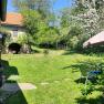 A green garden with flowering trees, a parasol, and an old building in the background.