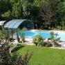 A covered outdoor pool with sun loungers and plants, surrounded by greenery.