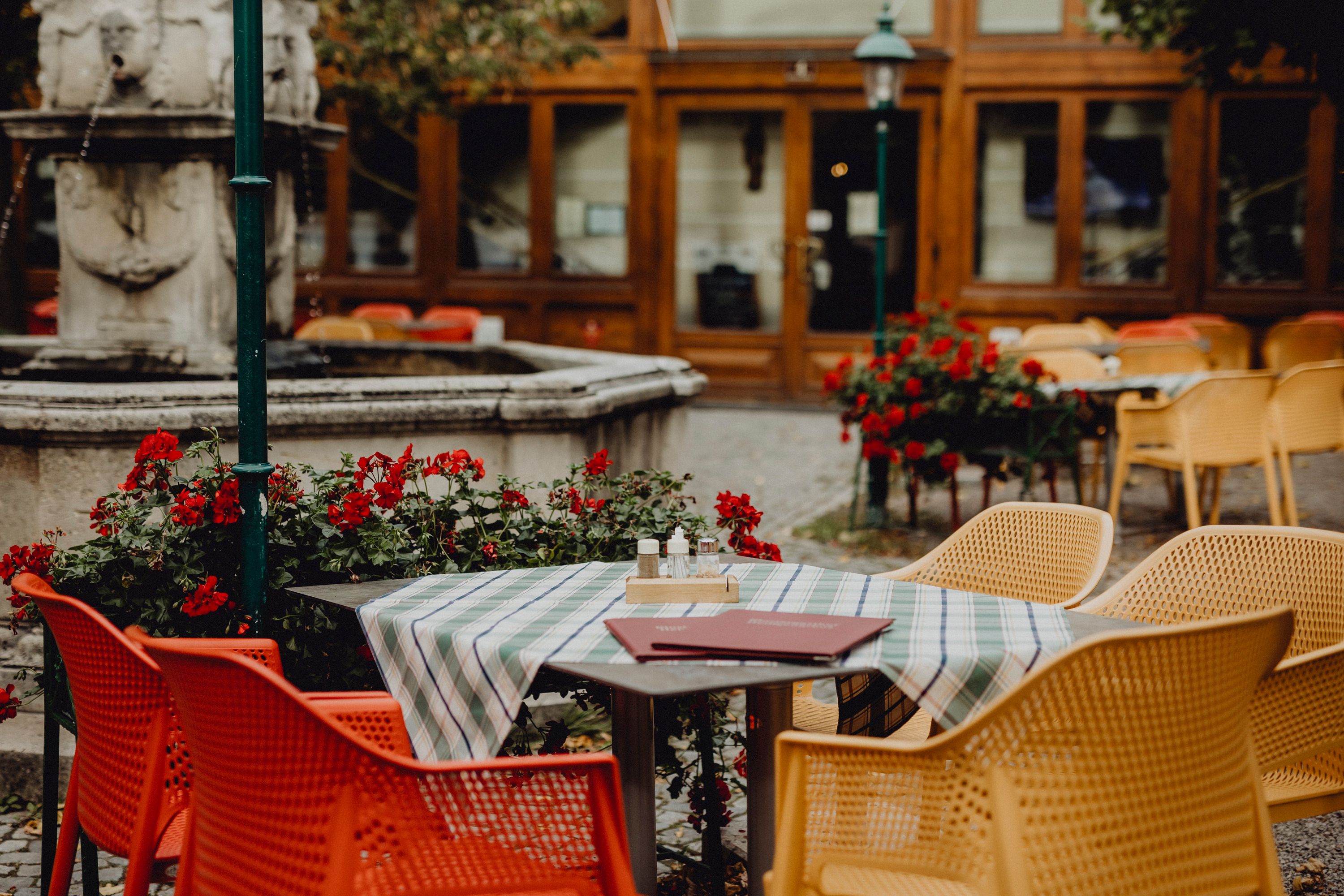 A guest garden with colorful chairs, a table with a tablecloth and a fountain in the background.