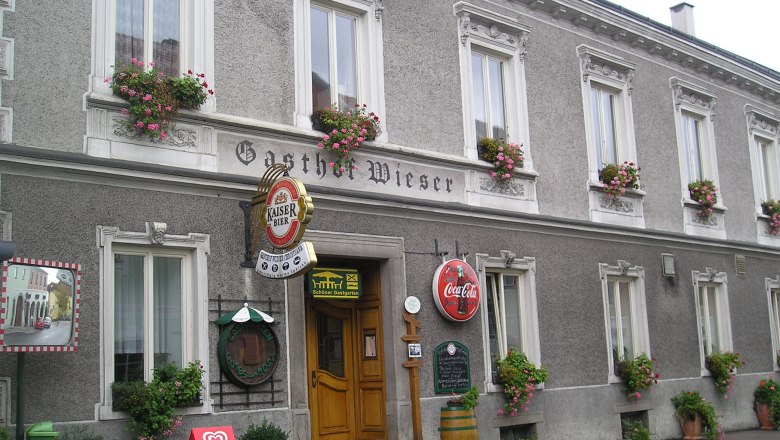 Facade of the Wieser inn with flower boxes and advertising signs.